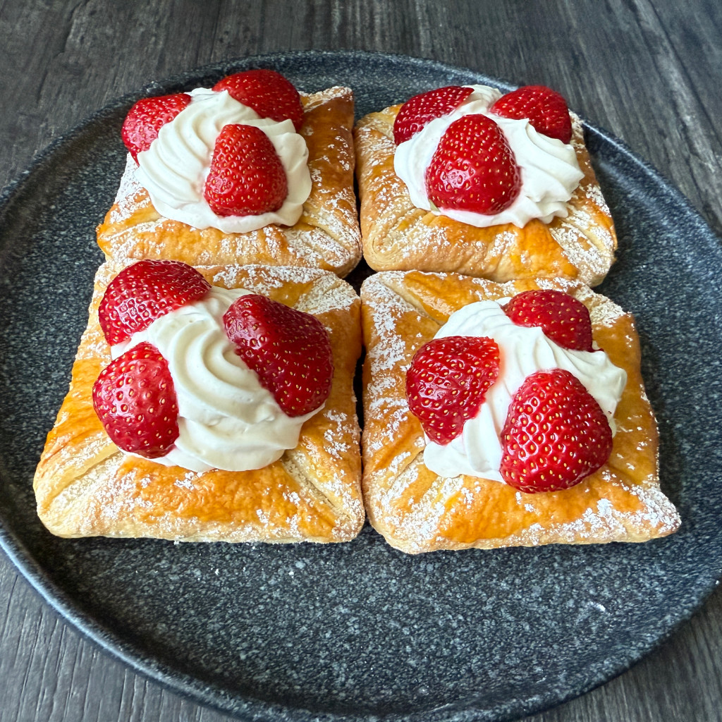 Goldbraun gebackene Erdbeerkörbchen aus Blätterteig, gefüllt mit heller Puddingsahne und garniert mit frischen Erdbeerstücken.
